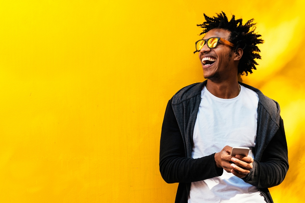 Happy young man with afro laughing in sunglasses against bright yellow wall