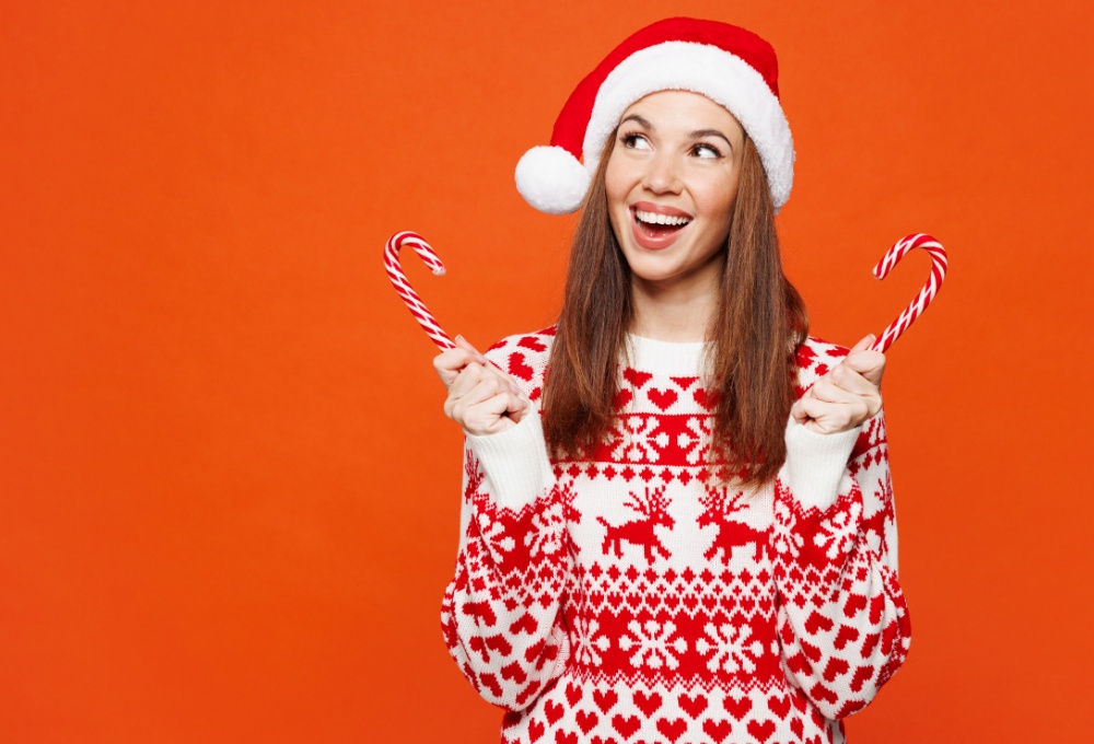 Joyful young woman in festive holiday sweater with two candy canes