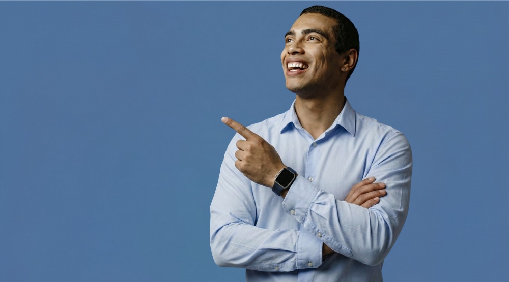Smiling Man in Blue Shirt Pointing Upward on Blue Background