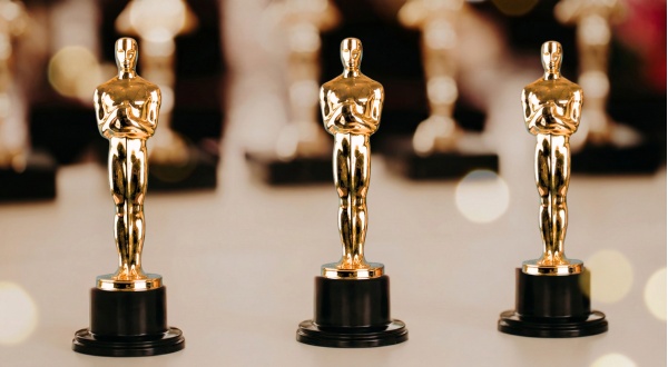 Three Golden Oscar statuettes in a row with black bases.