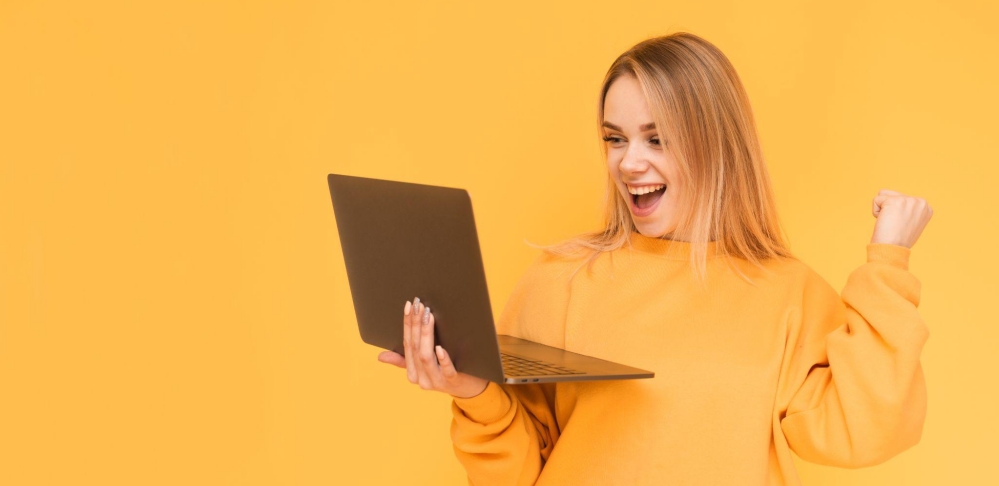 Excited woman with laptop celebrating success on bright orange background.