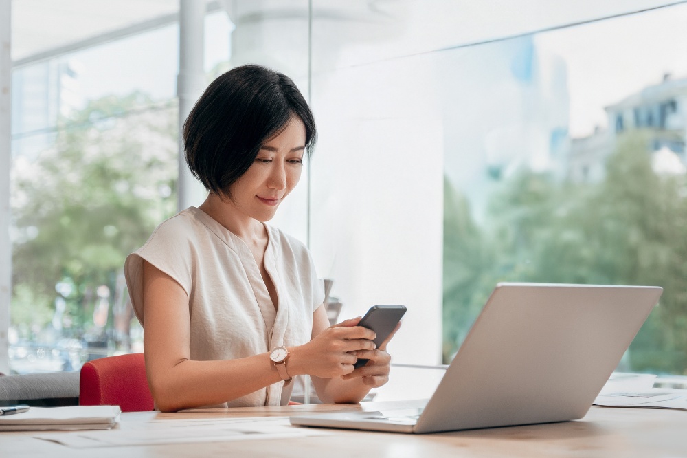 Professional woman using laptop and smartphone in modern office