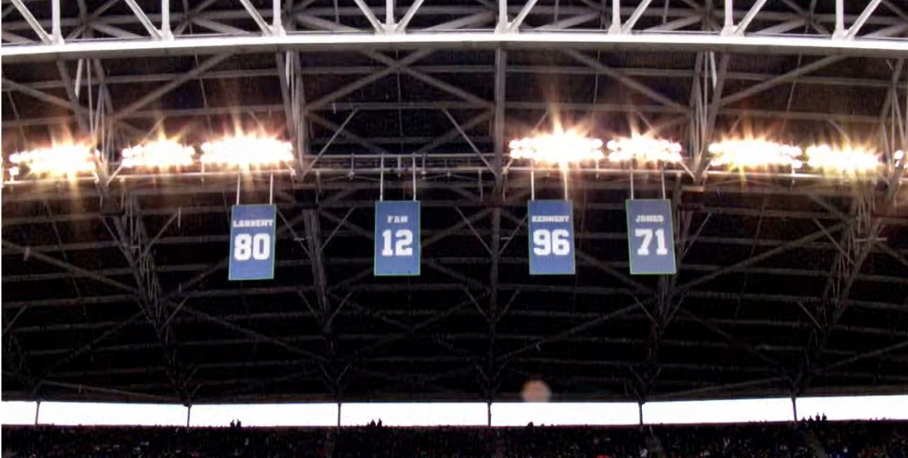 Retired numbers banners: Largent 80, Fan 12, Kennedy 96, Jones 71 in stadium rafters.