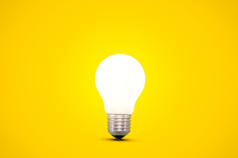 Glowing white light bulb on bright yellow background