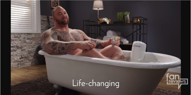 Tattooed man relaxing in bathtub holding drink in ad