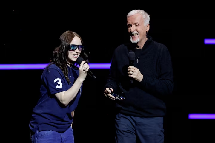 Two people laughing on stage holding microphones at a live event
