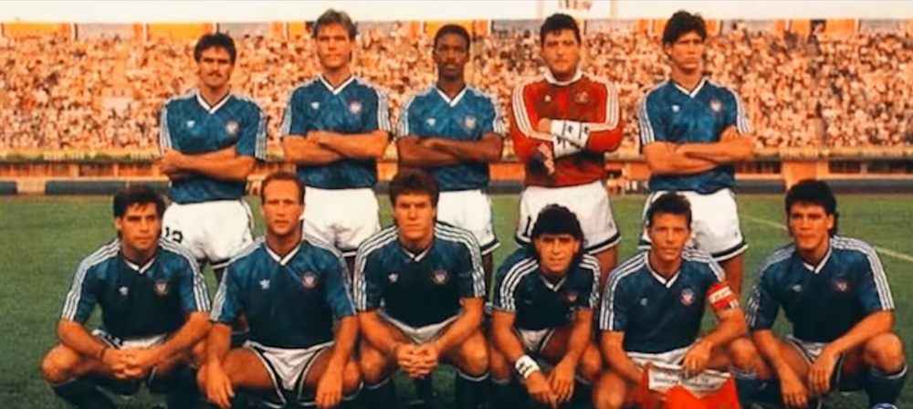 Soccer team posing in blue uniforms with goalkeeper in red at stadium