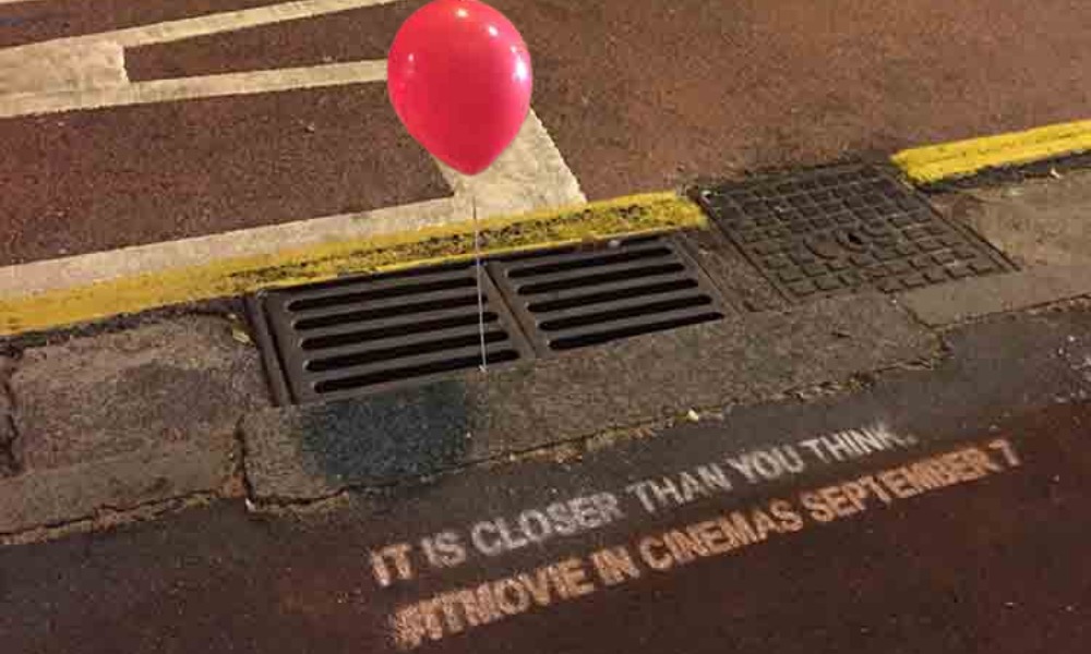 IT Movie guerrilla ad with red balloon tied to street drain at night