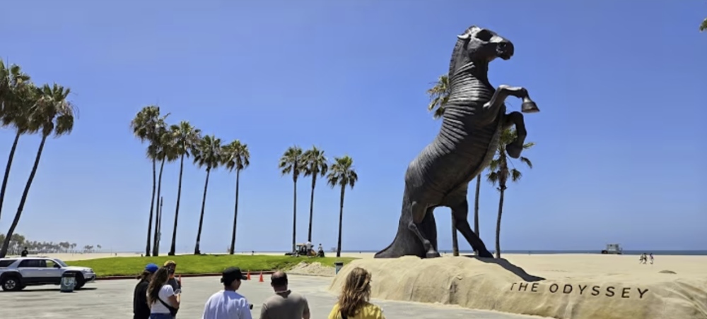 Giant bronze horse statue "The Odyssey" towers over beachfront palms.