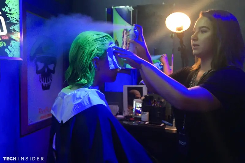 Stylist applies green hair dye under blue lighting backstage