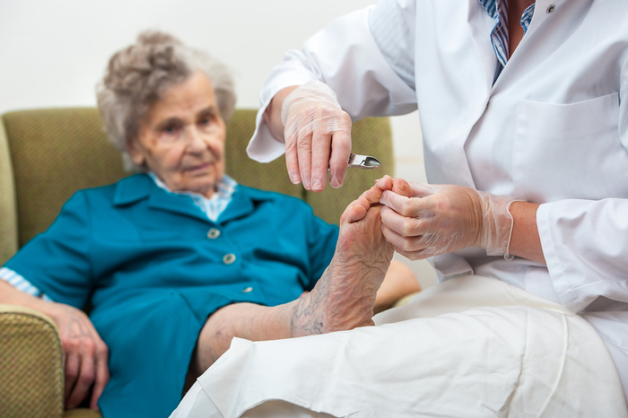 Elderly woman sitting in chair having her toenails clipped.