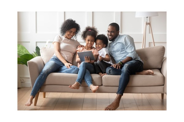Family sitting on a couch looking at a tablet together.
