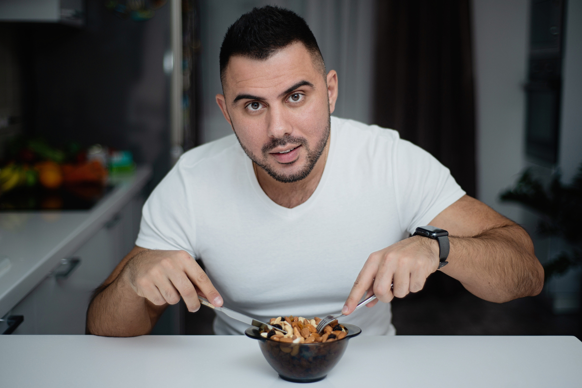 Man sitting at a table eating nuts from a bowl.