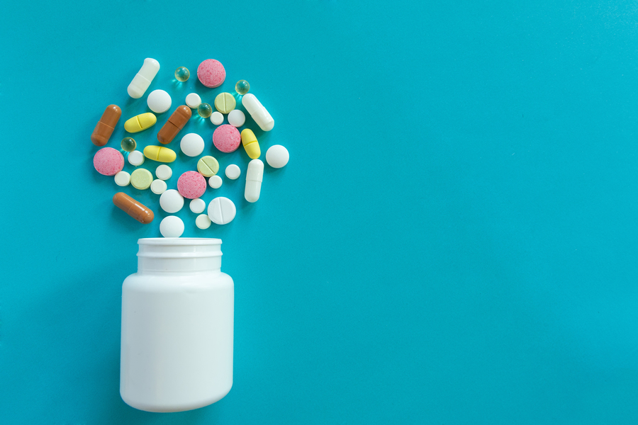 Pill bottle on its side with various medications spilling out.