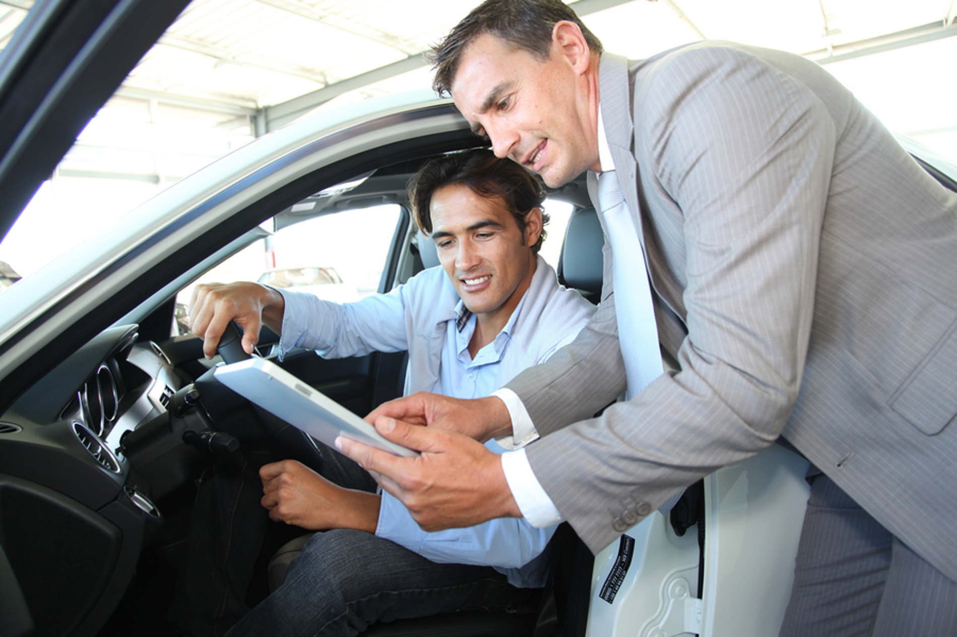 Man sitting in a new car speaking with a car salesman.