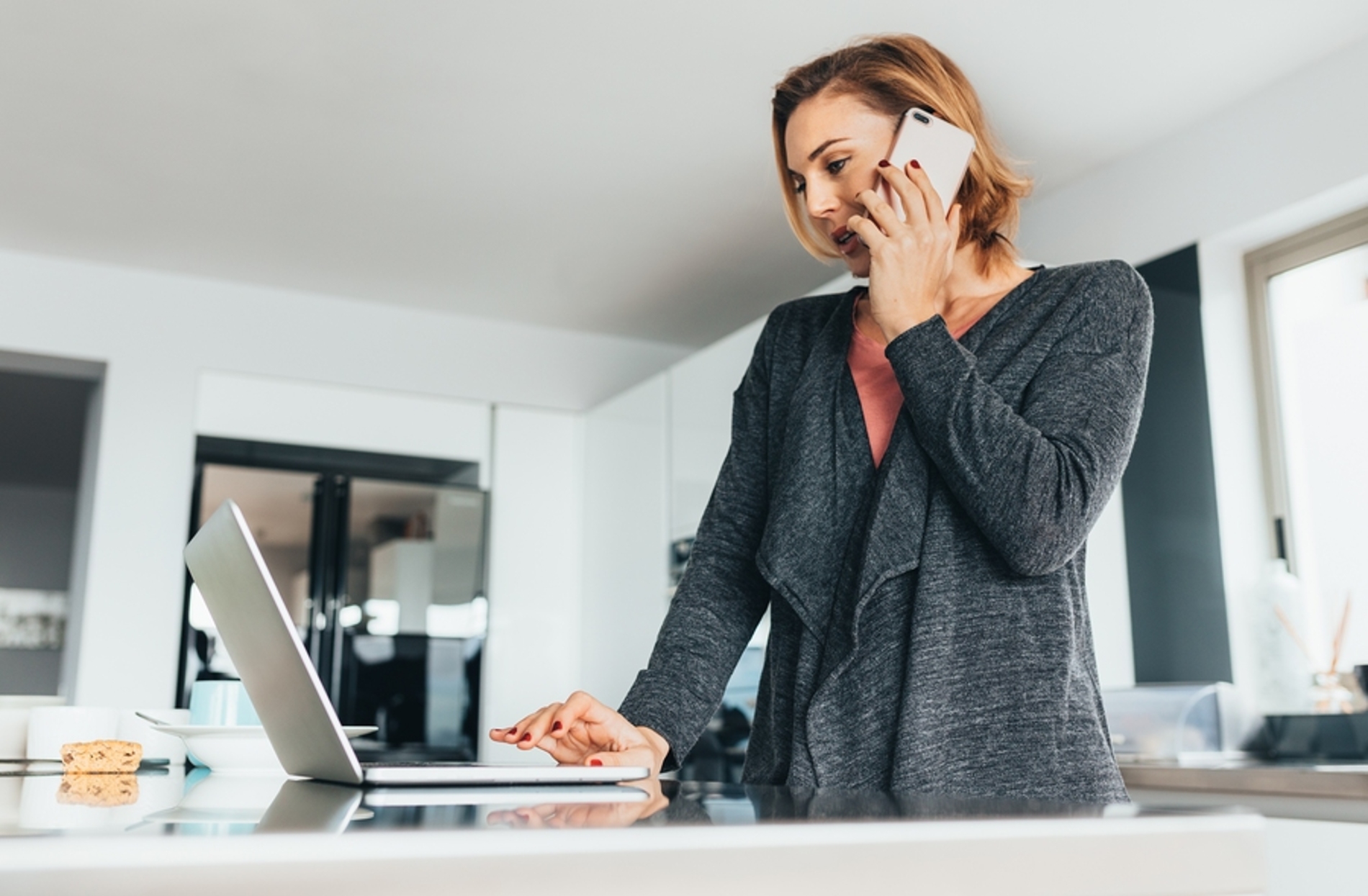 Woman talking on the phone while typing on a laptop computer.