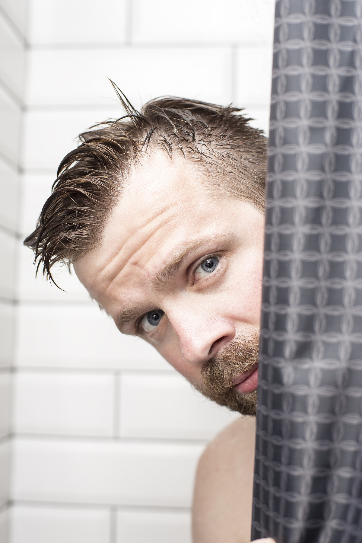 Man peeking out from behind a shower curtain.