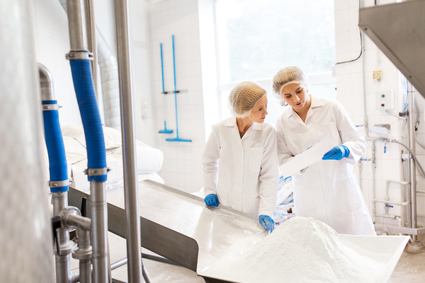 Two woman working in a factory with white coats and blue protective gloves.
