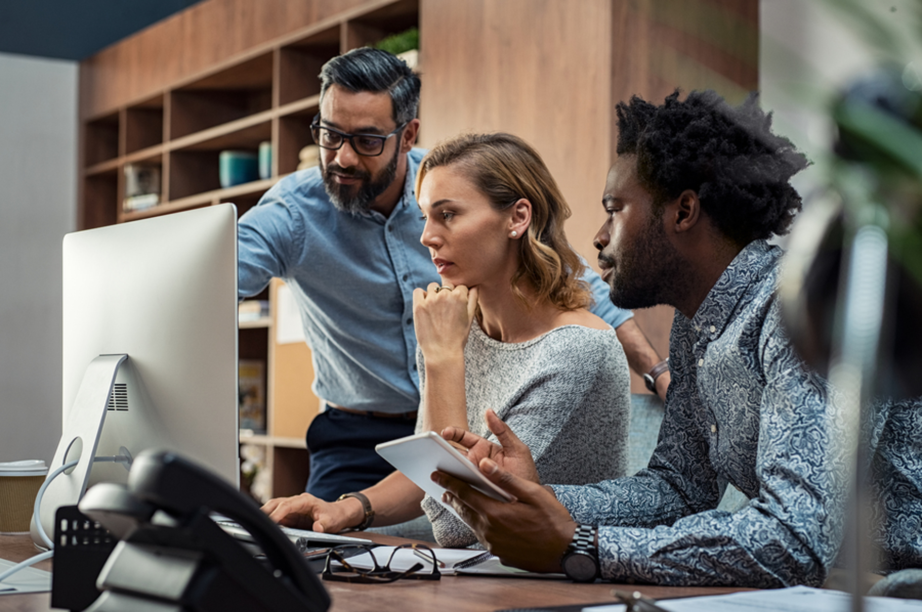 Three colleagues discussing a project over a desktop computer.