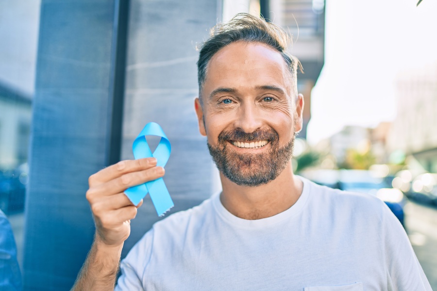 Smiling man holding a blue ribbon.
