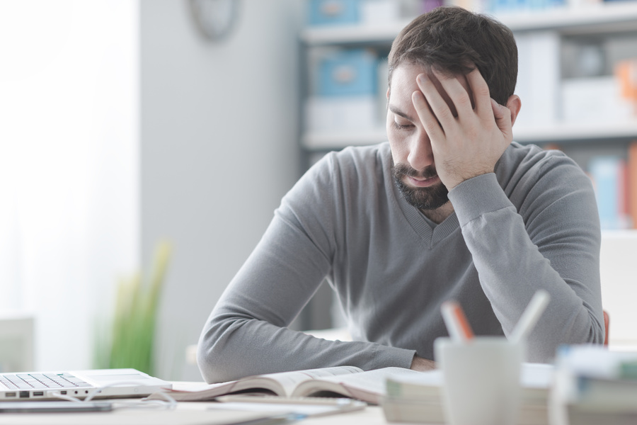 Man sitting at a table holding his head in his hand.