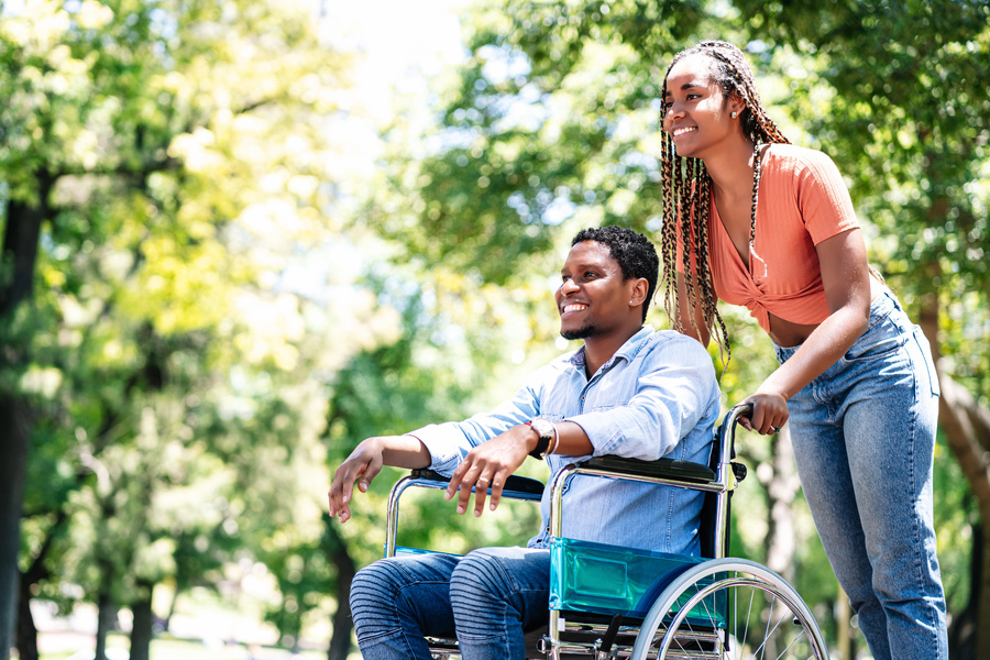 Woman pushing a man in a wheel chair outside.