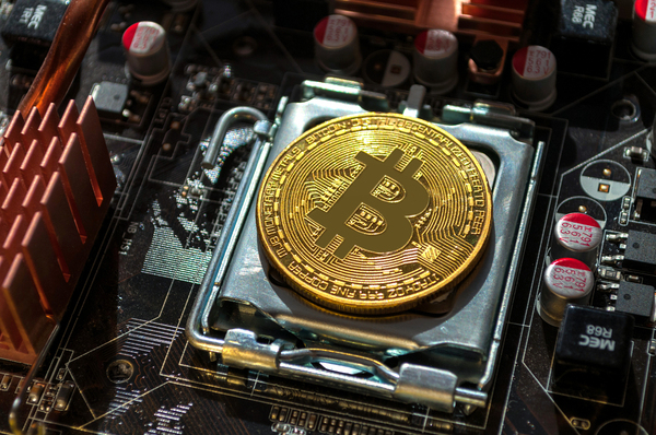 Gold coin with a bitcoin symbol on top of a computer motherboard.