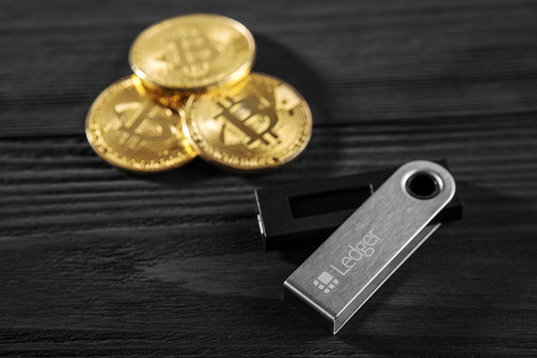 Three gold coins with bitcoin symbols and Ledger flash drive.