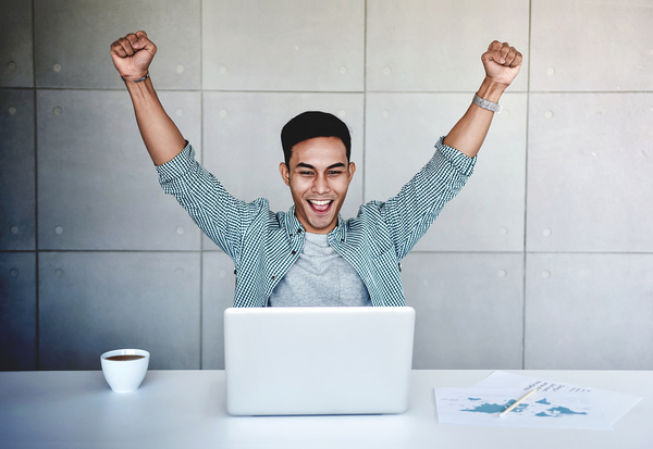 Man raising his hands up in triumph in front of a laptop computer.