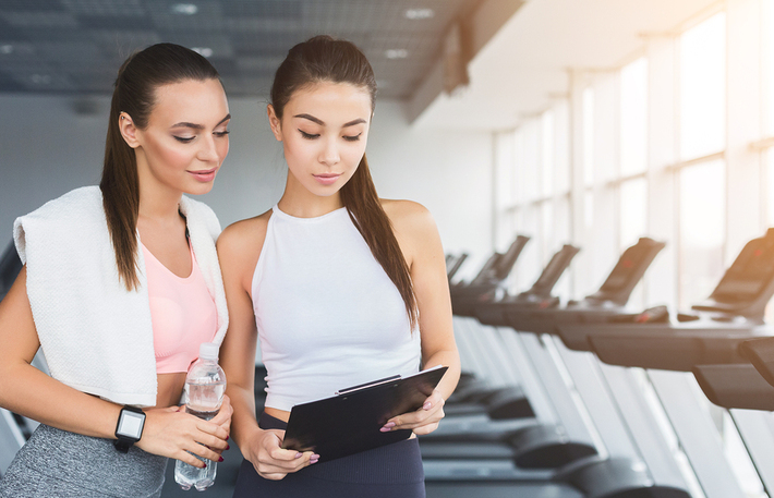 Two women looking at a document in a gym.