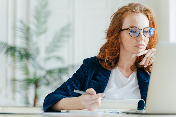 Woman looking intently at her computer screen while writing notes.