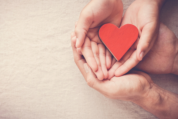 Wooden red heart in cupped hands.