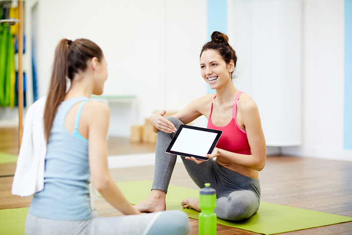 Two women at a gym looking at a tablet together.