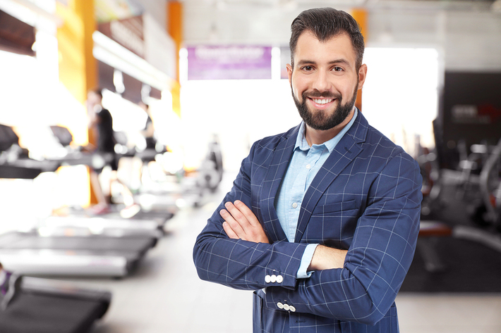 Man in a business suit smiling at a gym.