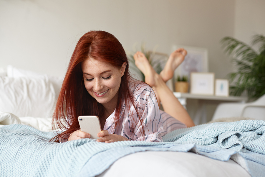 Woman lying on her bed looking at her phone.