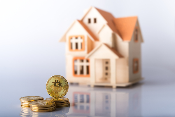 Miniature model of a home with gold coins that have bitcoin symbols.