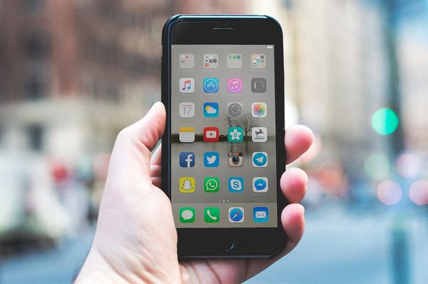 Person holding an iPhone with the home screen displayed.