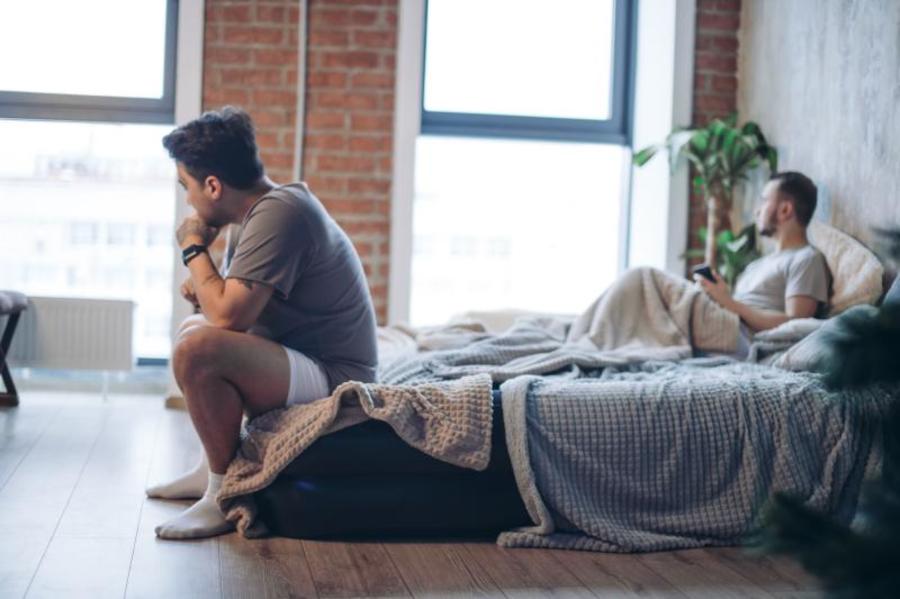 Man sitting at the edge of his bed appearing upset.