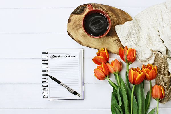 Tabletop with coffee, flowers and notebook with pen.