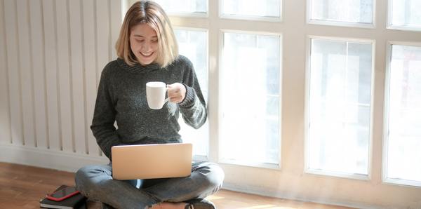 Smiling woman holding a cup of coffee and looking at her laptop screen.