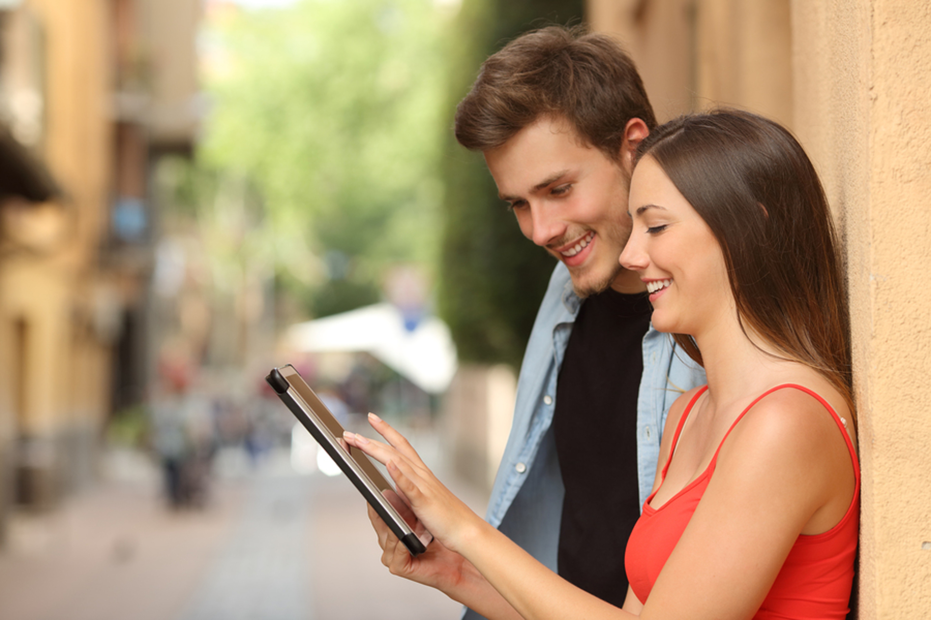Two people leaning against a well using a tablet to find local businesses. Two people leaning against a well using a tablet to find local businesses.