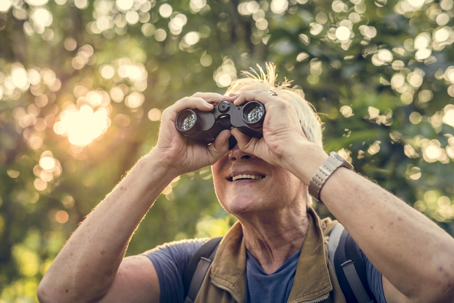 Elderly woman observing nature with binoculars.