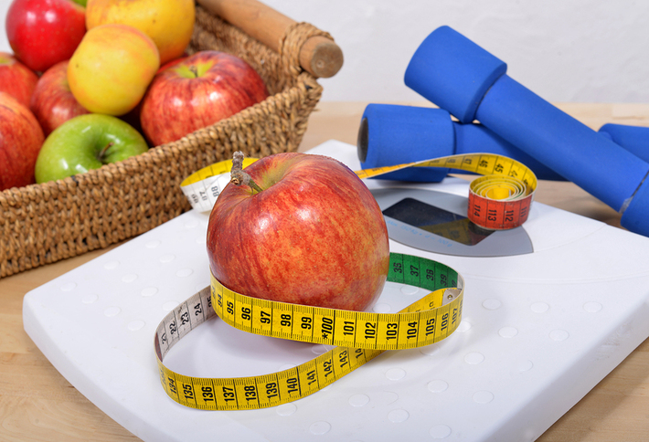 Basket with fruit, free weights and an apple surrounded by a tape measure.