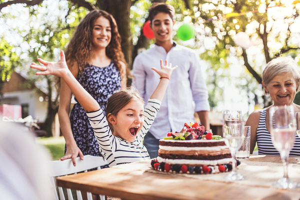 Young girl celebrating her birthday with a cake and family in the backyard.