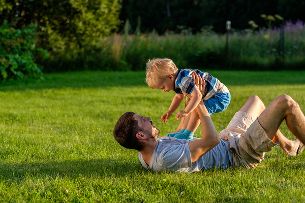 Father lying on the grass lifting his son up and both laughing.