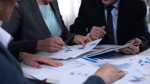 Group of colleagues sitting around a table looking at documents with charts and graphs.