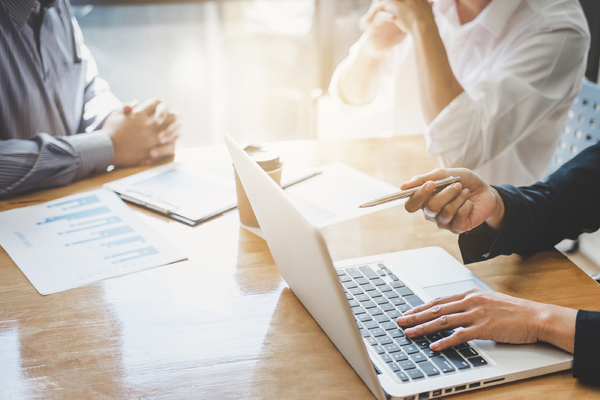 Three colleagues sitting at a table discussing information on documents and a laptop screen.