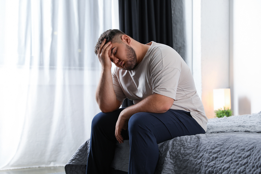 Man sitting at the edge of his bed appearing depressed.