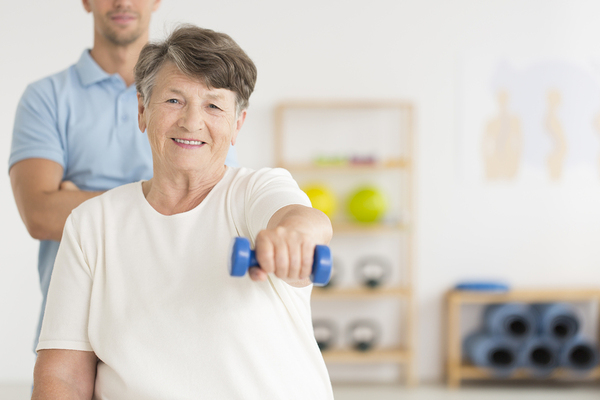 Older woman lifting weights with a physical therapist assisting.