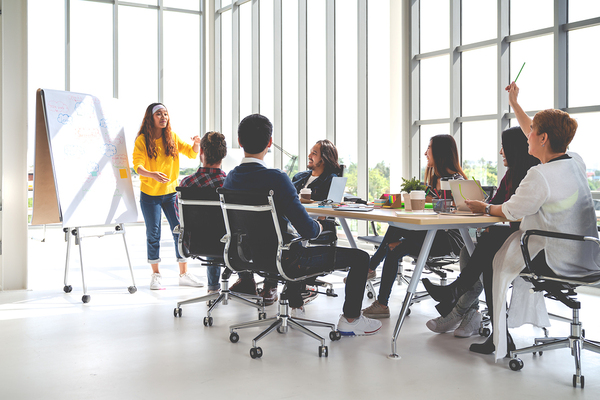 Woman presenting to a a group sitting around a conference table.